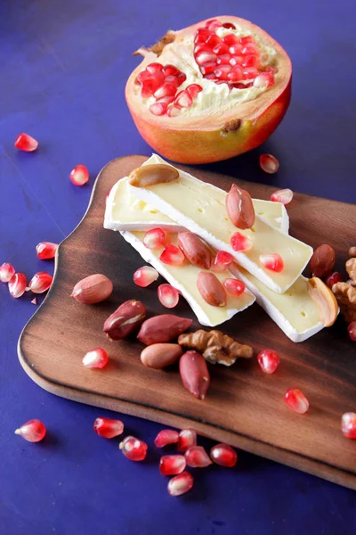 Camembert peyniri, peynir, fıstık, ceviz, nar taneleri retro tarzı ahşap oyun tahtası koyu mavi zemin üzerine dilimlenmiş