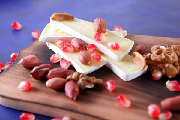 Camembert peyniri, peynir, fıstık, ceviz, nar taneleri retro tarzı ahşap oyun tahtası koyu mavi zemin üzerine dilimlenmiş