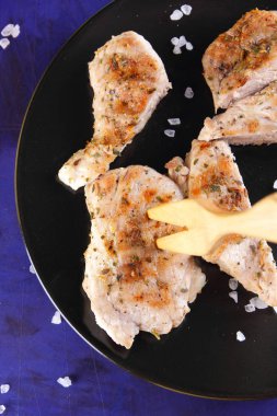 Biftek ahşap çatal, büyük tuz, baharat ve fıstık retro tarzı bir koyu mavi arka plan üzerinde siyah bir tabak ızgara ile