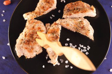 Biftek ahşap çatal, büyük tuz, baharat ve fıstık retro tarzı bir koyu mavi arka plan üzerinde siyah bir tabak ızgara ile