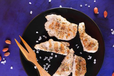 Biftek ahşap çatal, büyük tuz, baharat ve fıstık retro tarzı bir koyu mavi arka plan üzerinde siyah bir tabak ızgara ile