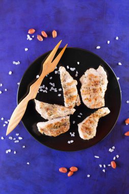 Biftek ahşap çatal, büyük tuz, baharat ve fıstık retro tarzı bir koyu mavi arka plan üzerinde siyah bir tabak ızgara ile