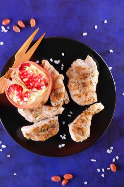 Biftek ahşap çatal, büyük tuz, baharat, nar ve fıstık retro tarzı bir koyu mavi arka plan üzerinde siyah bir tabak ızgara ile