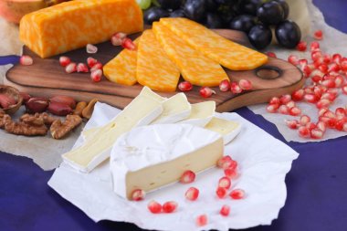 Camembert peyniri, mermer peynir, farklı peynirler, koyu mavi üzüm, kırmızı nar, Yeşil üzüm, fıstık ve ceviz ahşap oyun tahtası ile yazmak için boş bir yer