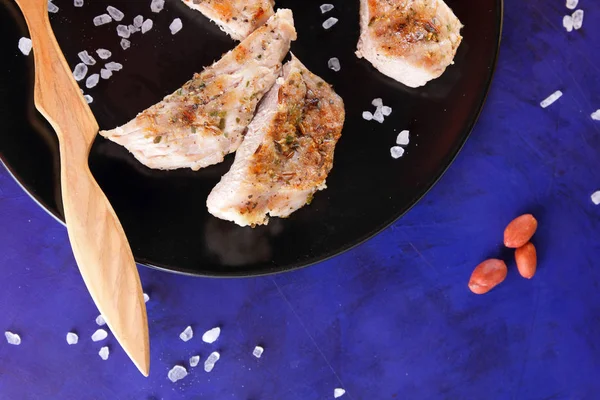 Biftek ahşap çatal, büyük tuz, baharat ve fıstık retro tarzı bir koyu mavi arka plan üzerinde siyah bir tabak ızgara ile