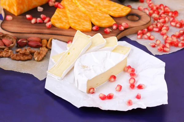Camembert peyniri, mermer peynir, farklı peynirler, koyu mavi üzüm, kırmızı nar, Yeşil üzüm, fıstık ve ceviz ahşap oyun tahtası ile yazmak için boş bir yer