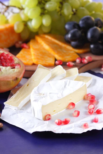 Camembert-Käse, marmorierter Käse, verschiedene Käsesorten, dunkelblaue Trauben, roter Granatapfel, grüne Trauben, Erdnüsse und Walnüsse auf einer Holztafel mit einer leeren Stelle zum Schreiben — Stockfoto