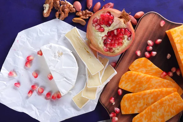 Camembert peyniri, mermer peynir, farklı peynirler, koyu mavi üzüm, kırmızı nar, Yeşil üzüm, fıstık ve ceviz ahşap oyun tahtası ile yazmak için boş bir yer