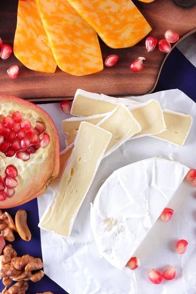 Camembert peyniri, mermer peynir, farklı peynirler, koyu mavi üzüm, kırmızı nar, Yeşil üzüm, fıstık ve ceviz ahşap oyun tahtası ile yazmak için boş bir yer
