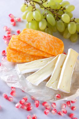 Camembert peyniri, dilimlenmiş peynir, turuncu peynir, peynir bir sürü. Yeşil üzüm ve beyaz zemin üzerine nar taneleri
