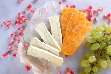 Camembert peyniri, dilimlenmiş peynir, turuncu peynir, peynir bir sürü. Yeşil üzüm ve beyaz zemin üzerine nar taneleri