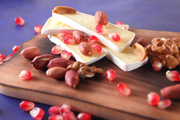 Camembert peyniri, peynir, fıstık, ceviz, nar taneleri ahşap oyun tahtası koyu mavi zemin üzerine dilimlenmiş