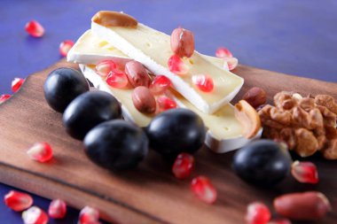 Camembert peyniri, peynir, fıstık, ceviz, nar taneleri ahşap oyun tahtası koyu mavi zemin üzerine dilimlenmiş