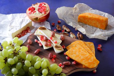 Camembert peyniri, turuncu sert peynir, Yeşil üzüm, fıstık, ceviz ve nar tohumları üzerinde koyu mavi arka plan retro tarzı ahşap bir gemide