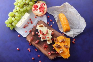 Camembert peyniri, turuncu sert peynir, Yeşil üzüm, fıstık, ceviz ve nar tohumları üzerinde koyu mavi arka plan retro tarzı ahşap bir gemide