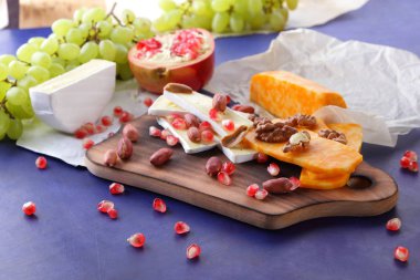 Camembert peyniri, turuncu sert peynir, Yeşil üzüm, fıstık, ceviz ve nar tohumları üzerinde koyu mavi arka plan retro tarzı ahşap bir gemide