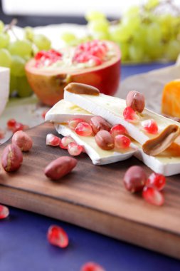 Camembert peyniri, turuncu sert peynir, Yeşil üzüm, fıstık, ceviz ve nar tohumları üzerinde koyu mavi arka plan retro tarzı ahşap bir gemide