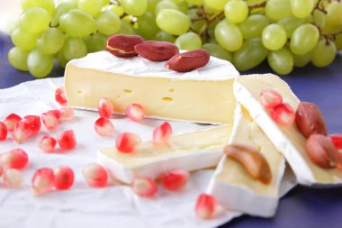 Camembert peyniri, peynir, peynir kalıp, Yeşil üzüm, fıstık ve nar taneleri ile Etiketler için koyu mavi zemin üzerine dilimlenmiş