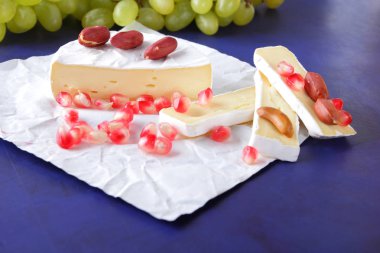 Camembert peyniri, peynir, peynir kalıp, Yeşil üzüm, fıstık ve nar taneleri ile Etiketler için koyu mavi zemin üzerine dilimlenmiş