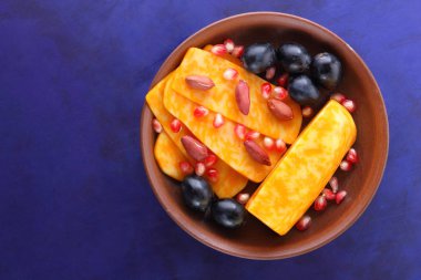 Turuncu peynir, peynir, bir çeşit sert peynir, mermer peynir, koyu mavi üzüm, fıstık ve nar taneleri retro tarzında bir kil plaka koyu mavi zemin üzerine dilimlenmiş