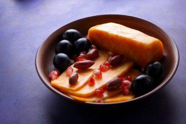 Turuncu peynir, peynir, bir çeşit sert peynir, mermer peynir, koyu mavi üzüm, fıstık ve nar taneleri retro tarzında bir kil plaka koyu mavi zemin üzerine dilimlenmiş