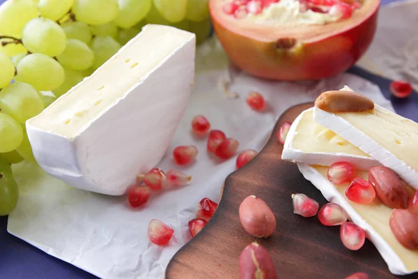 Camembert peyniri, turuncu sert peynir, Yeşil üzüm, fıstık, ceviz ve nar tohumları üzerinde koyu mavi arka plan retro tarzı ahşap bir gemide