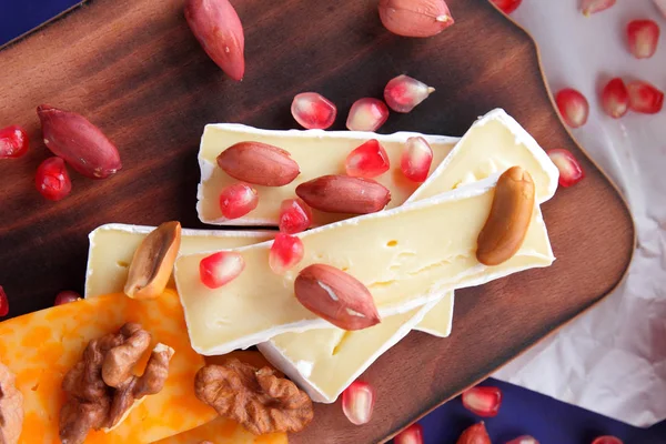 Camembert peyniri, turuncu sert peynir, Yeşil üzüm, fıstık, ceviz ve nar tohumları üzerinde koyu mavi arka plan retro tarzı ahşap bir gemide