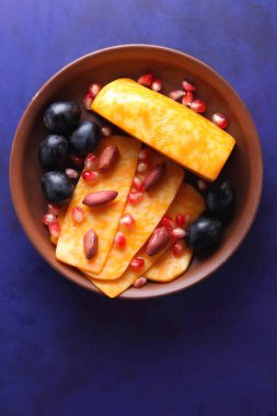 Turuncu peynir, peynir, bir çeşit sert peynir, mermer peynir, koyu mavi üzüm, fıstık ve nar taneleri retro tarzında bir kil plaka koyu mavi zemin üzerine dilimlenmiş