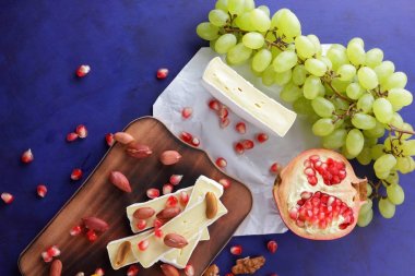 Camembert peyniri, turuncu sert peynir, Yeşil üzüm, fıstık, ceviz ve nar tohumları bir ahşap tahta üzerinde koyu mavi bir arka plan üzerinde