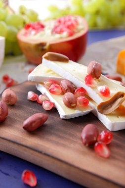 Camembert peyniri, turuncu sert peynir, Yeşil üzüm, fıstık, ceviz ve nar tohumları bir ahşap tahta üzerinde koyu mavi bir arka plan üzerinde