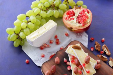 Camembert peyniri, turuncu sert peynir, Yeşil üzüm, fıstık, ceviz ve nar tohumları bir ahşap tahta üzerinde koyu mavi bir arka plan üzerinde