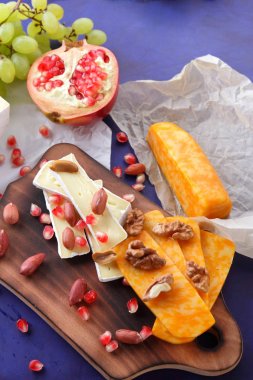 Camembert peyniri, turuncu sert peynir, Yeşil üzüm, fıstık, ceviz ve nar tohumları bir ahşap tahta üzerinde koyu mavi bir arka plan üzerinde