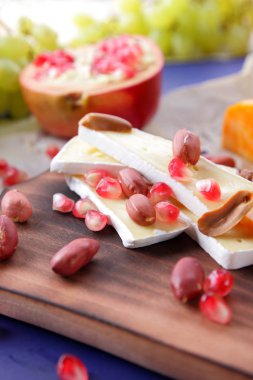 Camembert peyniri, turuncu sert peynir, Yeşil üzüm, fıstık, ceviz ve nar tohumları bir ahşap tahta üzerinde koyu mavi bir arka plan üzerinde