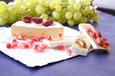 Camembert peyniri, peynir, peynir kalıp, Yeşil üzüm, fıstık ve nar taneleri ile koyu mavi bir arka plan dilimlenmiş
