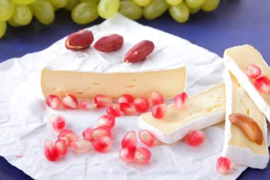 Camembert peyniri, peynir, peynir kalıp, Yeşil üzüm, fıstık ve nar taneleri ile koyu mavi bir arka plan dilimlenmiş