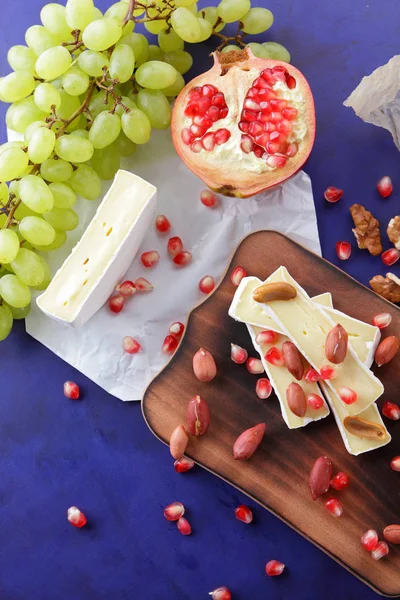 Camembert peyniri, turuncu sert peynir, Yeşil üzüm, fıstık, ceviz ve nar tohumları bir ahşap tahta üzerinde koyu mavi bir arka plan üzerinde