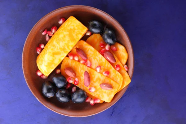 Turuncu peynir, peynir, bir çeşit sert peynir, mermer peynir, koyu mavi üzüm, fıstık ve nar taneleri bir kil plaka koyu mavi zemin üzerine dilimlenmiş