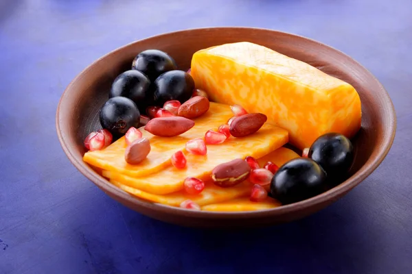 Turuncu peynir, peynir, bir çeşit sert peynir, mermer peynir, koyu mavi üzüm, fıstık ve nar taneleri bir kil plaka koyu mavi zemin üzerine dilimlenmiş