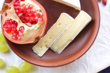 Camembert peyniri, bir bardak kefir, nar, çilek, Yeşil üzüm, fıstık tahıl ve beyaz ve koyu mavi zemin üzerine ekmek