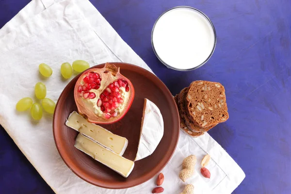 Camembert peyniri, bir bardak kefir, nar, çilek, Yeşil üzüm, fıstık tahıl ve beyaz ve koyu mavi zemin üzerine ekmek