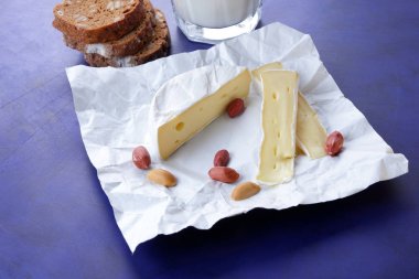Camembert peyniri, bir bardak süt, nar, fıstık tahıl ve beyaz kumaş üzerine ekmek ve koyu mavi arka plan