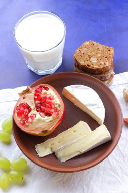 Camembert peyniri, bir bardak kefir, nar, çilek, Yeşil üzüm, fıstık tahıl ve retro tarzı içinde beyaz ve koyu mavi zemin üzerine ekmek