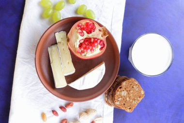Camembert peyniri, bir bardak kefir, nar, çilek, Yeşil üzüm, fıstık tahıl ve retro tarzı içinde beyaz ve koyu mavi zemin üzerine ekmek
