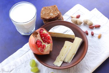 Camembert peyniri, bir bardak kefir, nar, çilek, Yeşil üzüm, fıstık tahıl ve retro tarzı içinde beyaz ve koyu mavi zemin üzerine ekmek