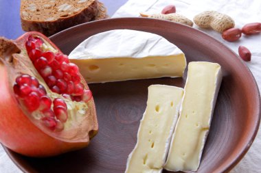 Camembert peyniri, bir bardak süt, nar, fıstık tahıl ve beyaz kumaş üzerine ekmek ve retro tarzı bir koyu mavi arka plan