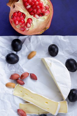 Camembert peyniri, bir bardak süt, nar, fıstık tahıl ve beyaz kumaş üzerine ekmek ve retro tarzı bir koyu mavi arka plan
