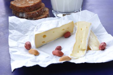 Camembert peyniri, bir bardak süt, nar, fıstık tahıl ve beyaz kumaş üzerine ekmek ve retro tarzı bir koyu mavi arka plan