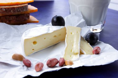 Camembert peyniri, turuncu mermer peynir, süt, nar, zeytin, fıstık tahıl, koyu mavi üzüm ve ekmek beyaz kumaş ve koyu mavi arka plan, peynir arka planda retro tarzı bir bardak