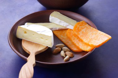 Camembert peyniri, turuncu peynir, fıstık, tahta kaşık ve spatula ile kil ware vintage tarzı bir koyu mavi arka plan üzerinde