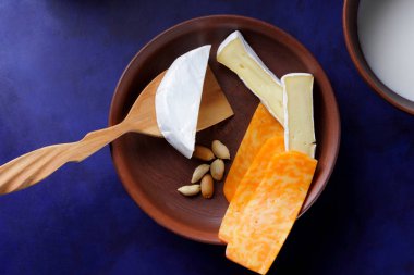 Camembert peyniri, turuncu peynir, fıstık, tahta kaşık ve spatula ile kil ware vintage tarzı bir koyu mavi arka plan üzerinde